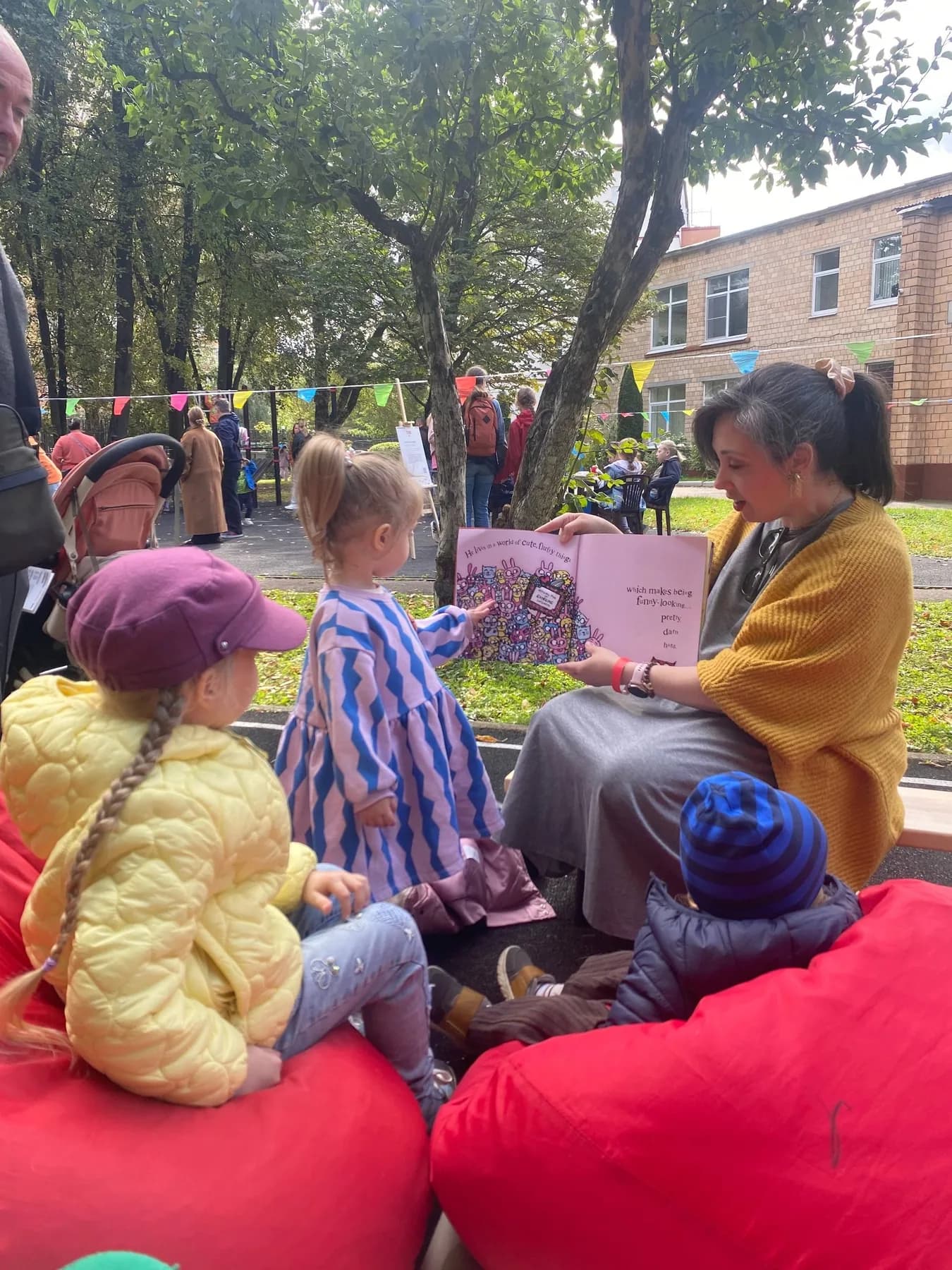 A woman reading an English picture book to children on red beanbags